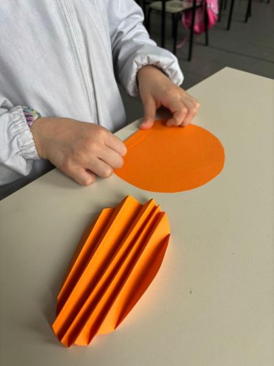 Un banco con un cerchio piegato a fisarmonica e mani di bambina che iniziano a piegare un secondo cerchio.
